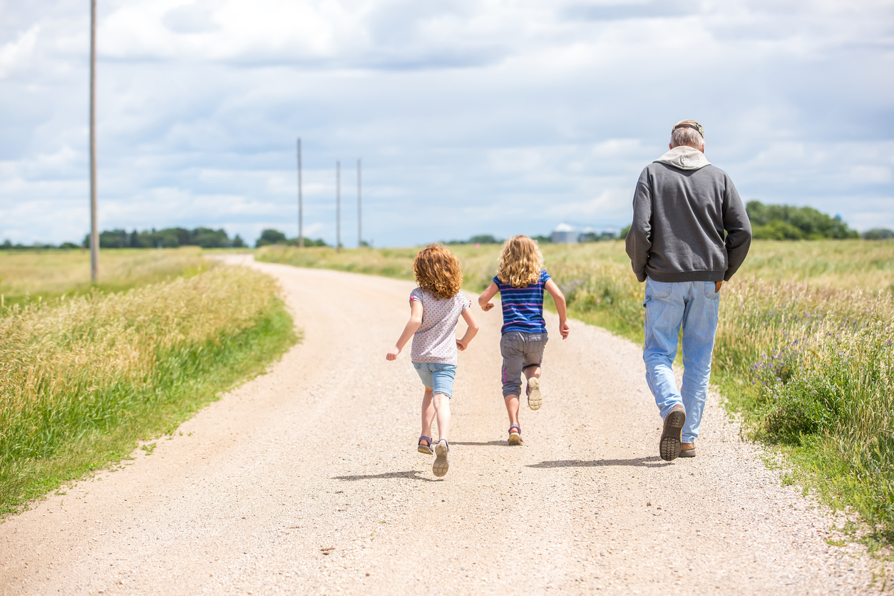 Older man and two young girls walking down a dirt road in rural Minnesota