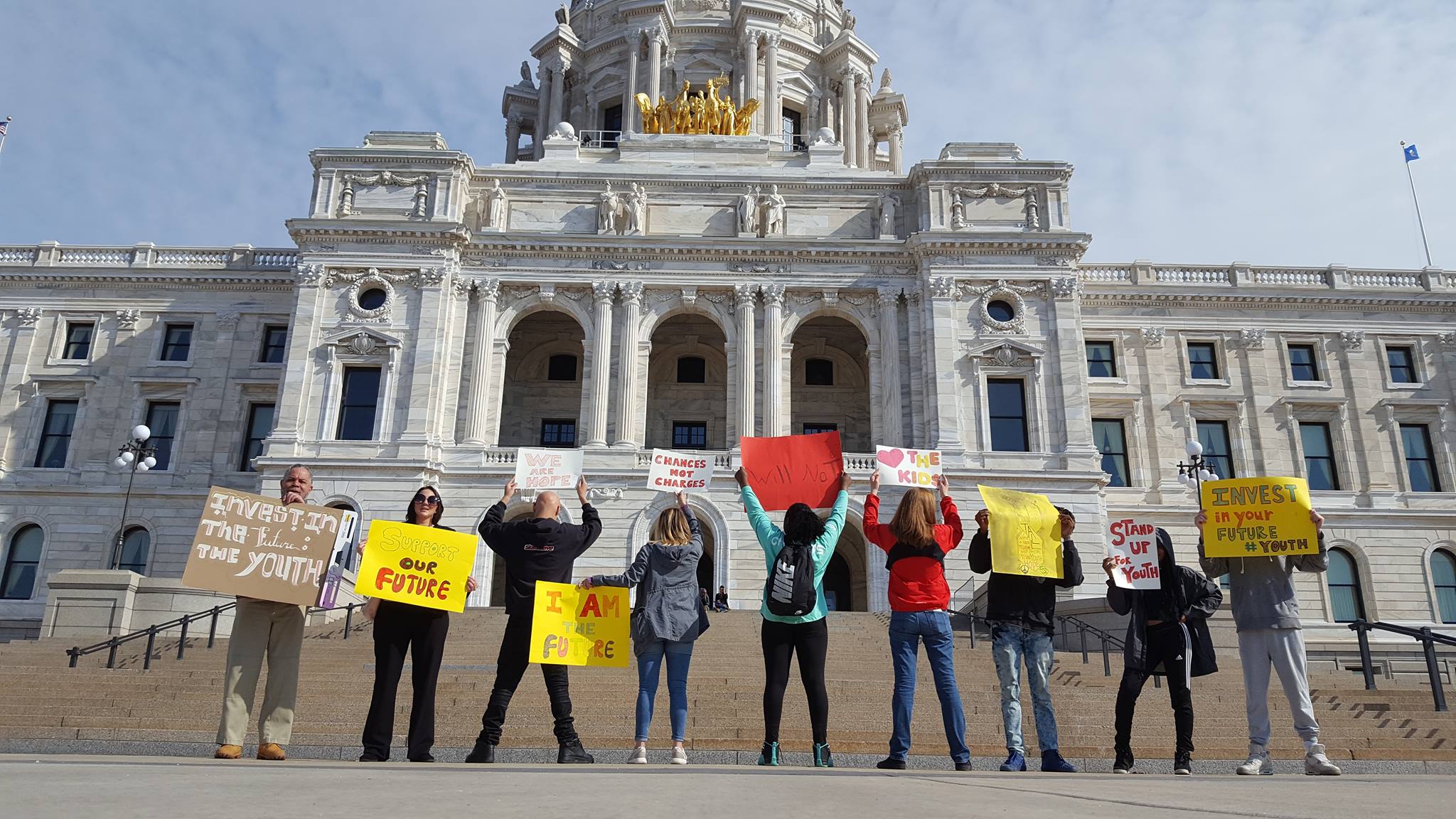 A group of youth leaders stand in front of the Minnesota State Capitol, holding signs that read, "Support our Future"