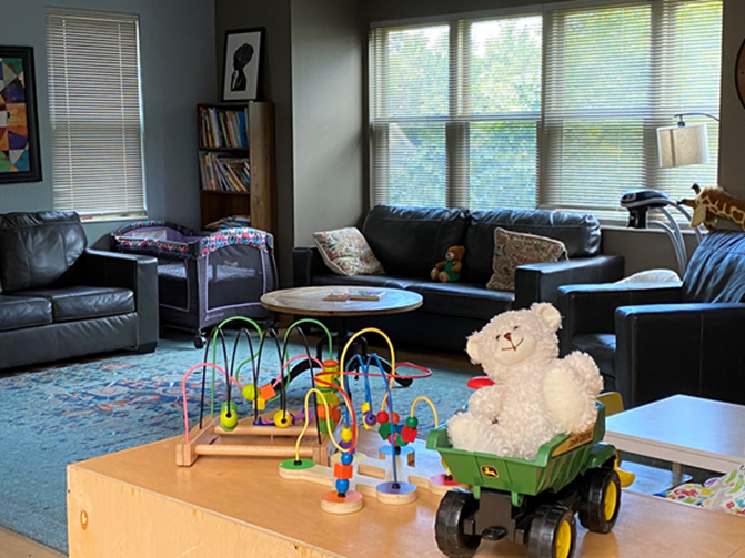 A room within Marlene's Place with windows, comfortable sofas, and children's toys