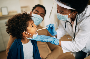 A child gets a throat exam in a doctor's office, while their parent holds them.