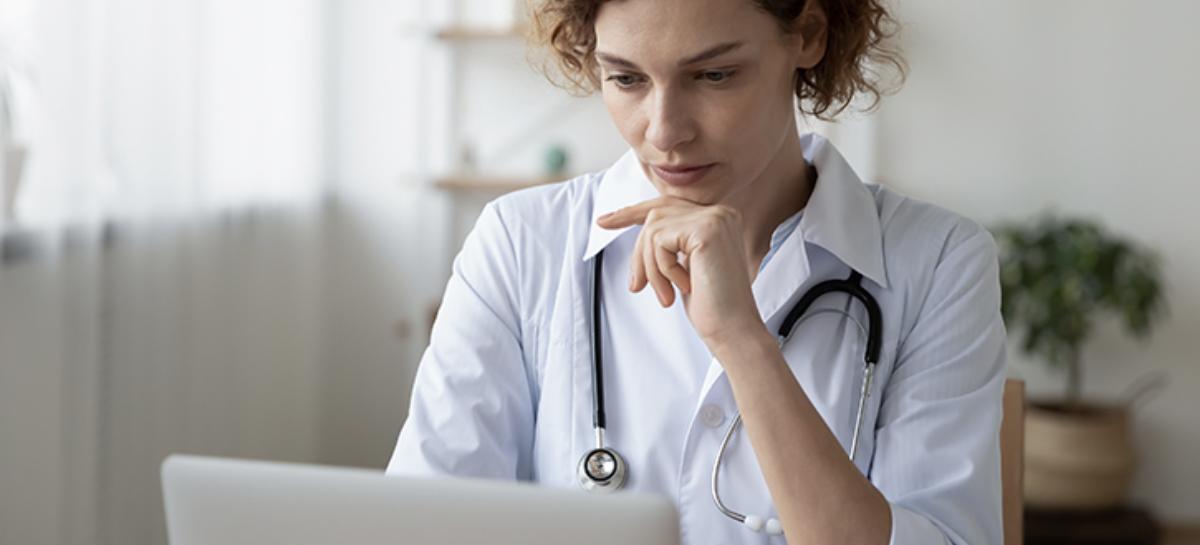 A researcher with a stethoscope around her neck looks at a laptop on the table in front of her