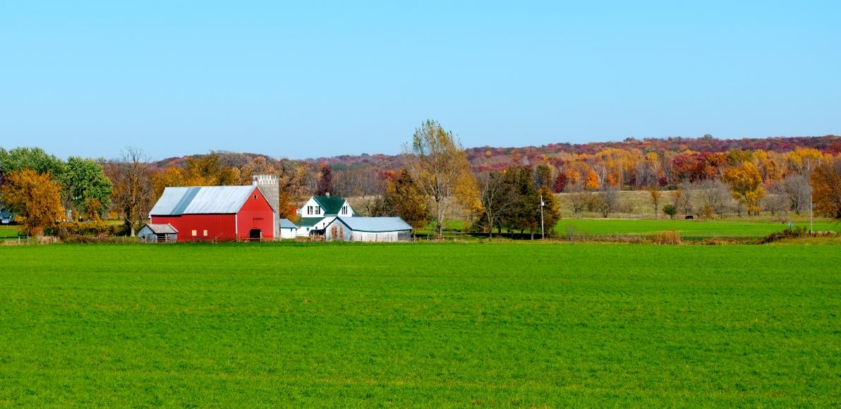 A landscape view of a red barn on a green lawn, with trees in the background.