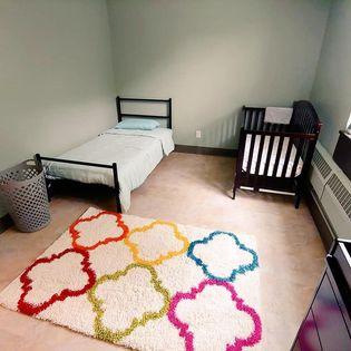 A bedroom within Gloria's place with a bed, crib, and colorful rug