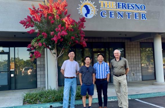 Boguang Sun, Por Choua, Tou Thao, and Dr. Straka stand in front of a building with a sign that says, "The Fresno Center." Left to right: Ph.D. student Boguang Sun, The Fresno Center’s Por Choua, Tou Thao, and Dr. Straka.